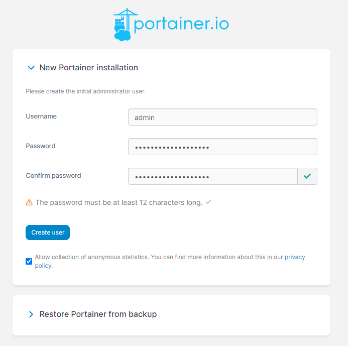 A login page showing three labels with three fields. The labels in order being Username, Password and Confirm Password with corresponding fields. There is also a warning after the three fields saying that a password must be at least 12 characters long. After that there is a blue button that says Create User, followed by a checkbox that asks whether you wish to provide anonymous user data for the Portainer developers and a link to their privacy policy. At the bottom of the picture is a fan menu that can open up labeled Restore Portainer from backup.