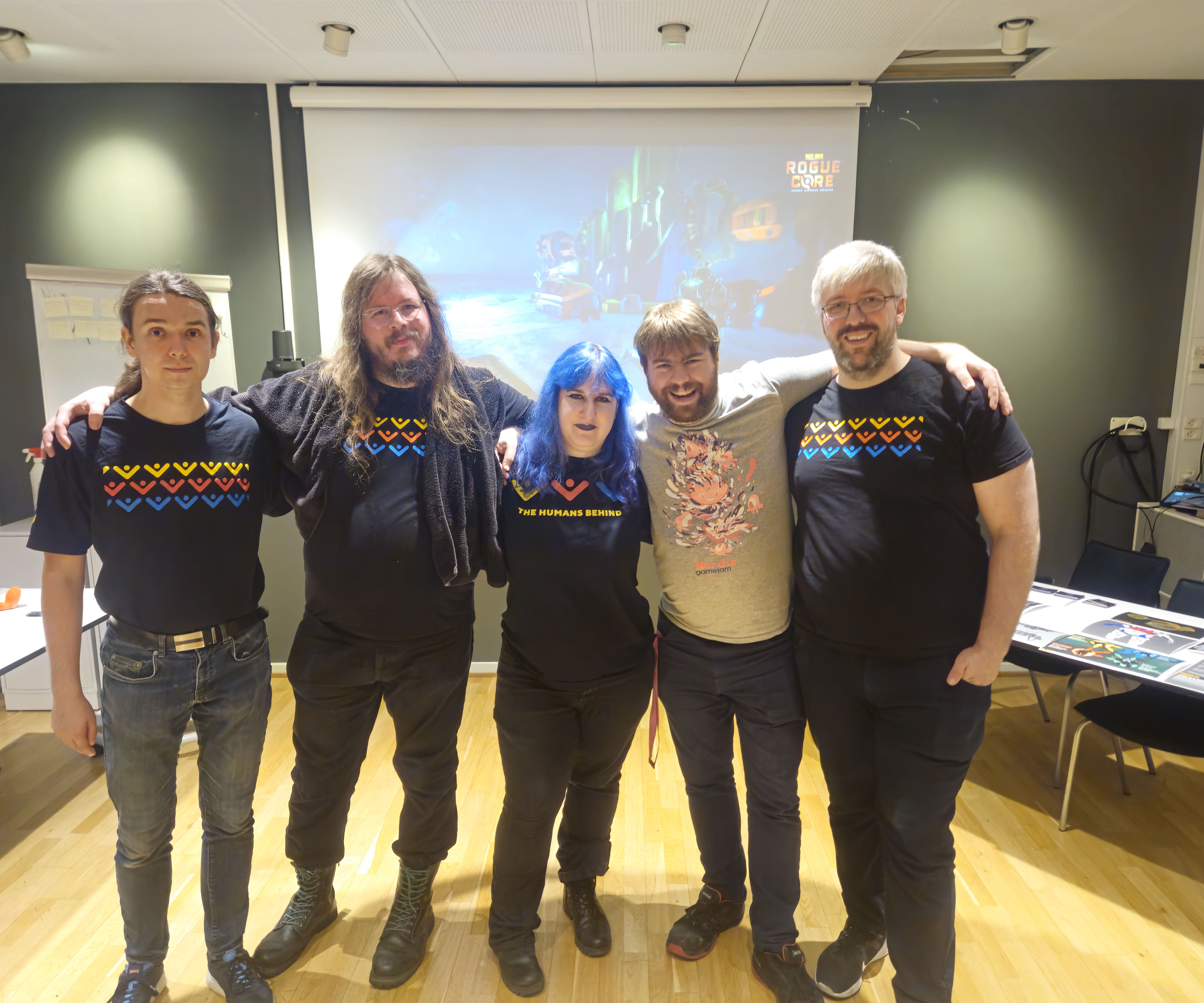 The five volunteers for Game Workers Guild that worked that worked the event today. From left to right is Andreas, who was participating extraordinarily today but is otherwise not involved, Allan, Lani who was the organiser of todays event, Kristian and myself, Mads. We are all wearing the Game Workers Guild tshirt which consists of yellow, red and blue abstractions of people putting their hands in the air.