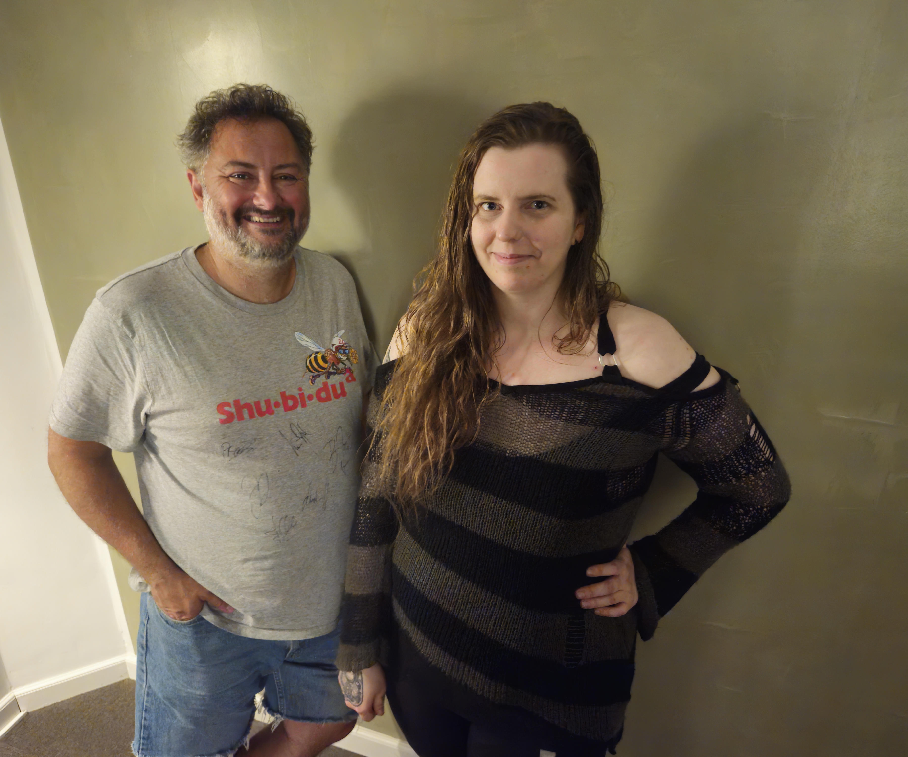 Thomas Gravgaard (Left) and Nathalie Michel (Right) standing up against a green wall smiling at the camera.