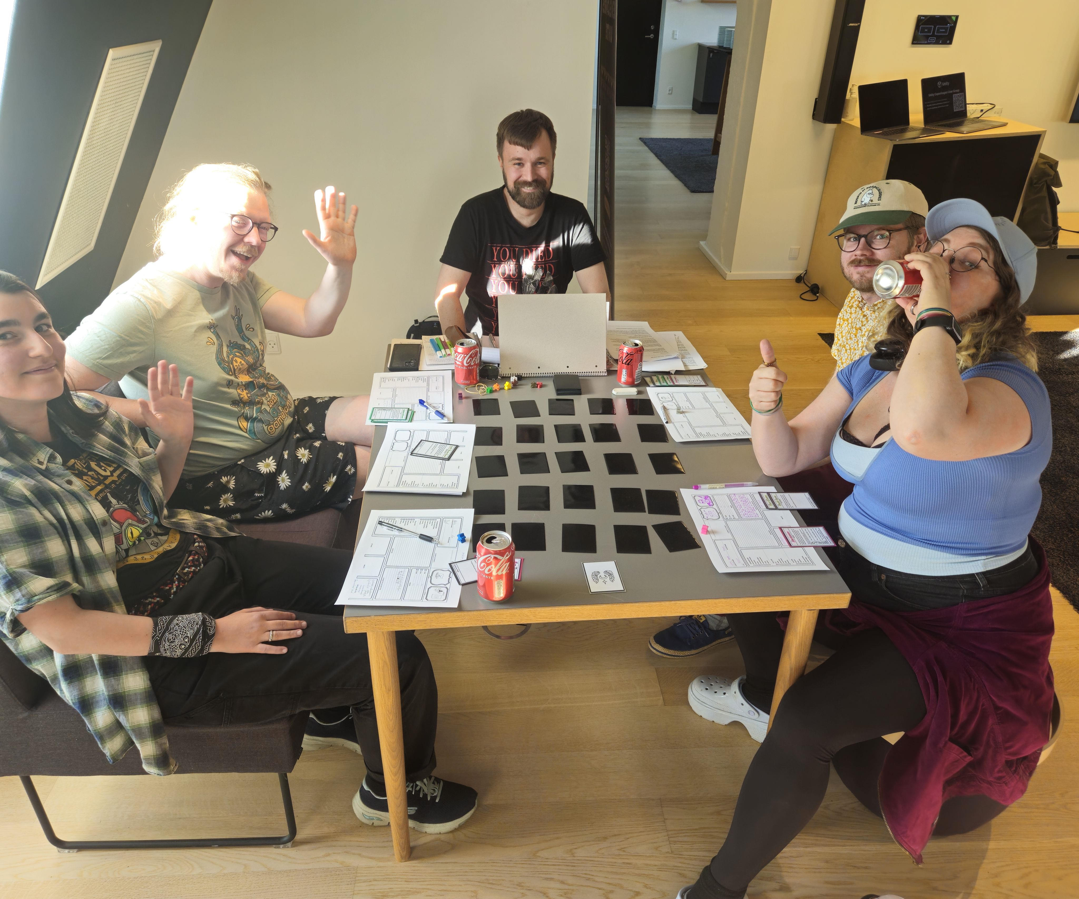 Four players sit around a table with their character sheets and in the middle are several black cards that needs to be flipped in order to see what's on the other side of them. At the end of the table sits the creator of the game doubling as a game master to control certain mechanical aspects and flow of the game.
