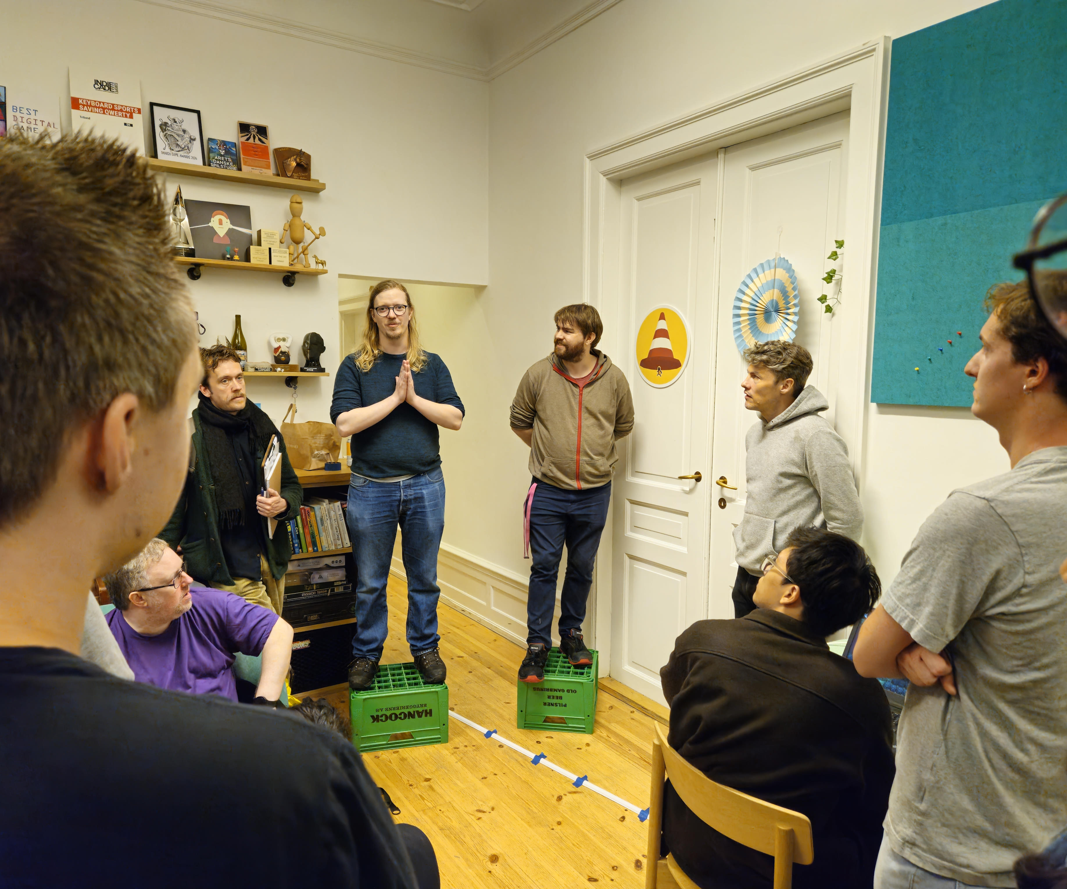Alex is in the left side of the image giving a welcome address to a room full of people ready to play games while Kristian stands to the right.