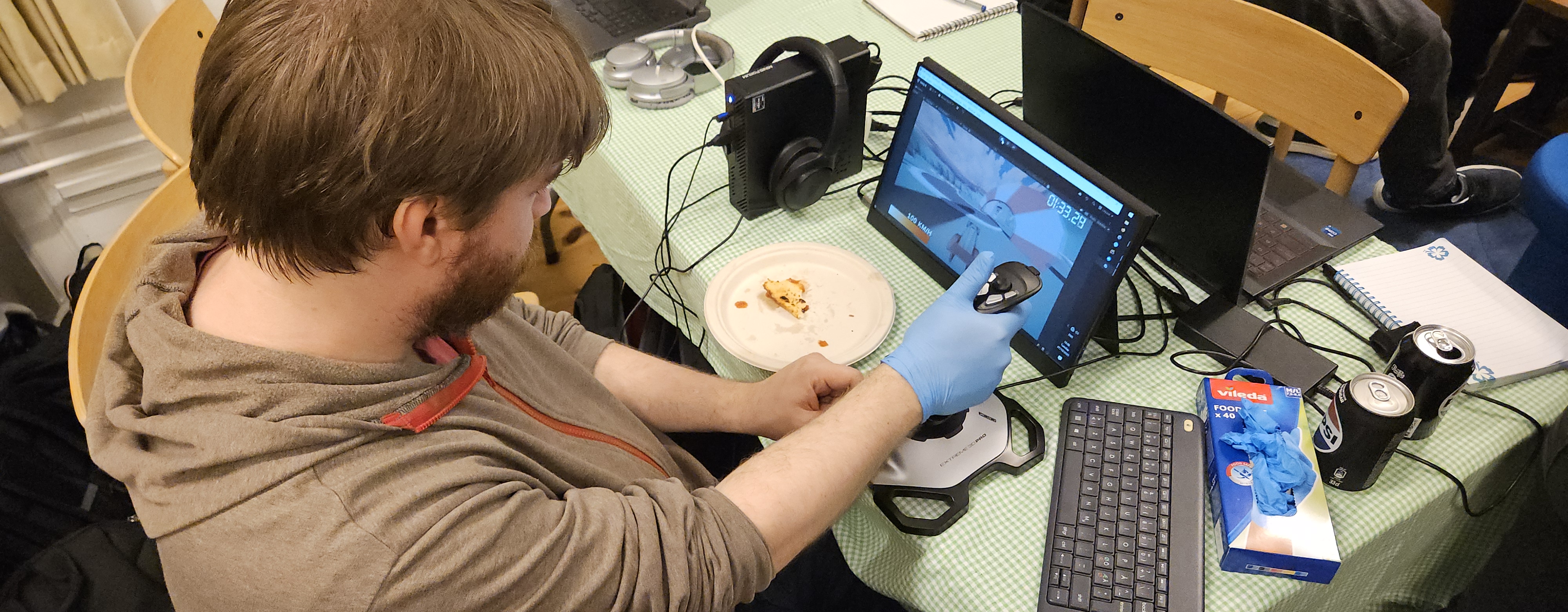 Kristian Hedeholm is concentrating deeply while he is sitting in front of a screen with a joystick controller in his right hand and his left hand is on a small throttle lever to control acceleration.
