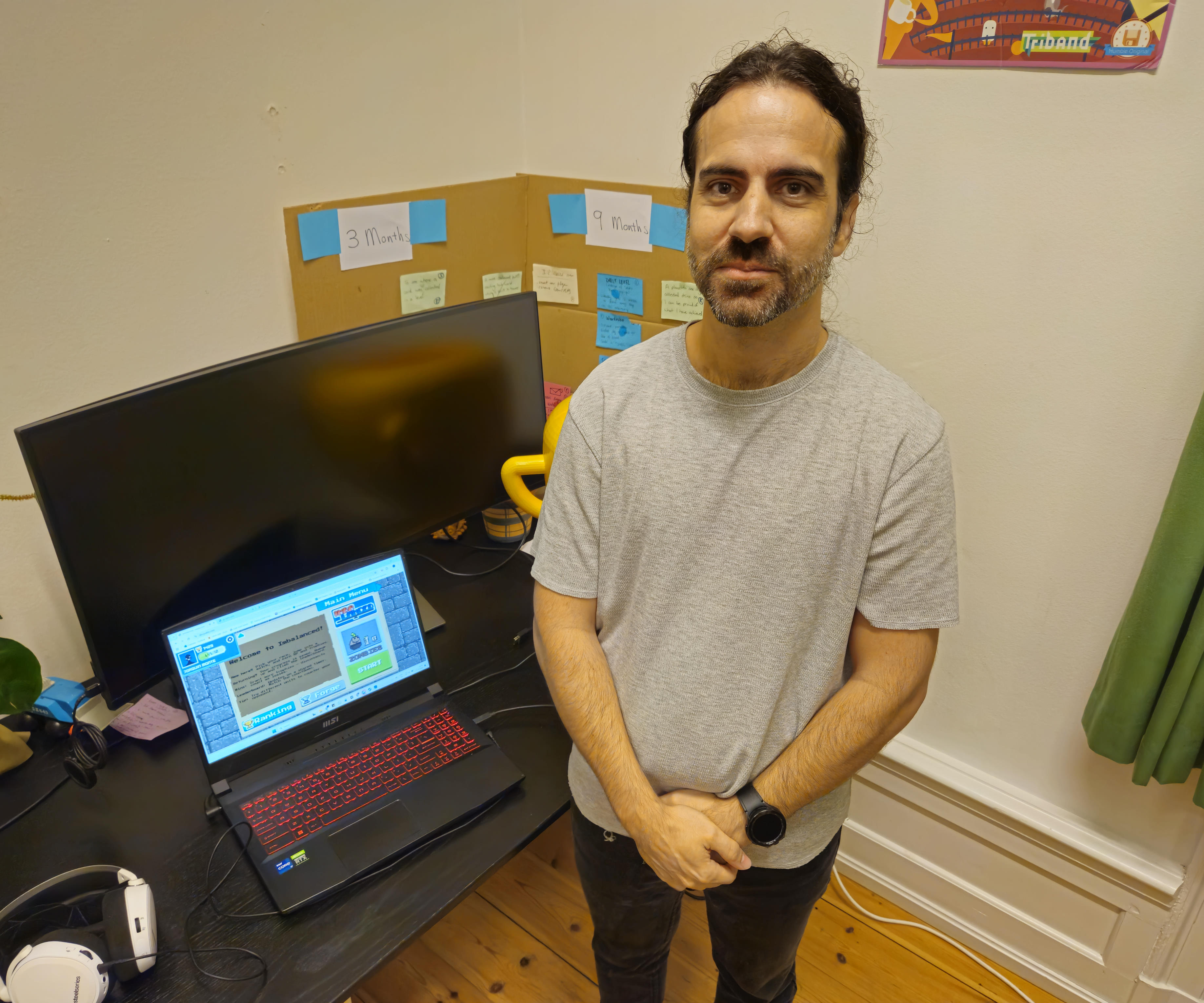 The developer Juaquin Monte standing to the right of his laptop showing the game's start screen.