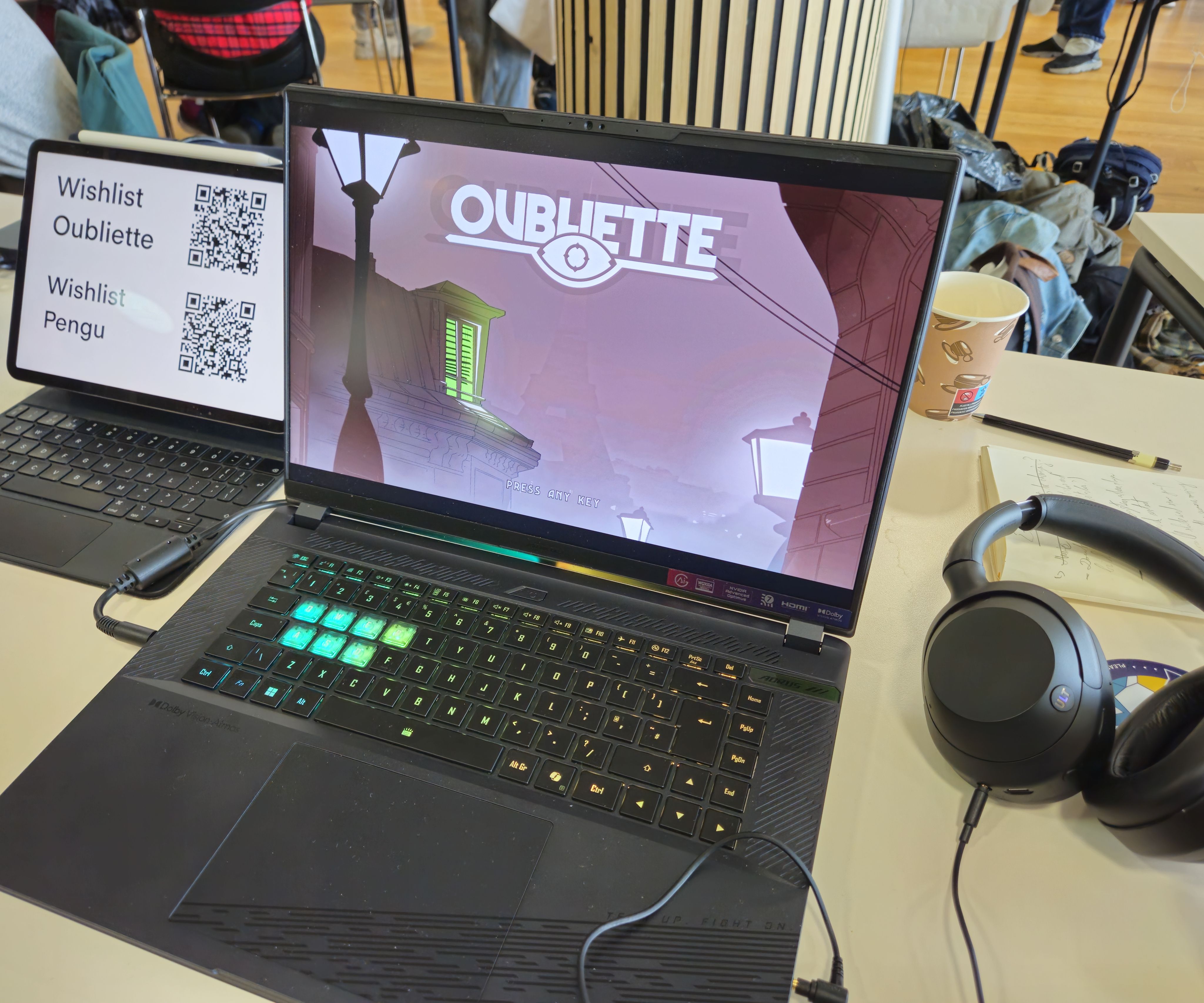 On a laptop is the title screen for the game showing old streets of a fictional city inspired by old British architecture covered in mist and eerie hues of purple and green.